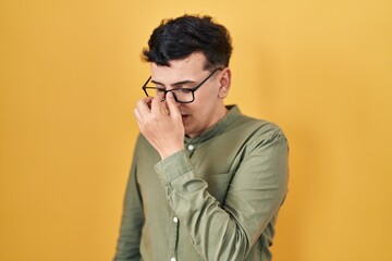 Non binary person standing over yellow background tired rubbing nose and eyes feeling fatigue and...
