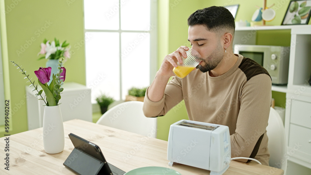 Sticker Young arab man having breakfast using touchpad at home