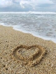 Heart shape on the beach sand beside the waves