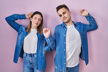 Obraz premium Young hispanic couple standing over pink background stretching back, tired and relaxed, sleepy and yawning for early morning