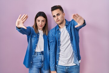 Young hispanic couple standing over pink background doing frame using hands palms and fingers, camera perspective