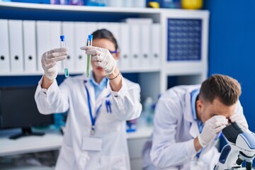 Man and woman scientists using microscope holding test tubes at laboratory