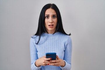 Hispanic woman using smartphone clueless and confused expression. doubt concept.