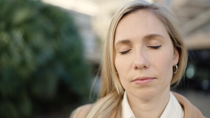 Obraz premium Young blonde woman breathing with closed eyes at park