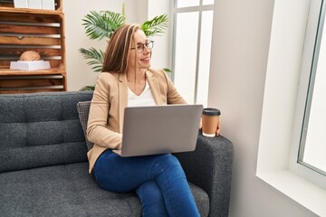 Young blonde woman psychologist using laptop drinking coffee at psychology clinic