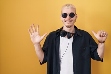 Young caucasian man wearing sunglasses standing over yellow background showing and pointing up with fingers number six while smiling confident and happy.