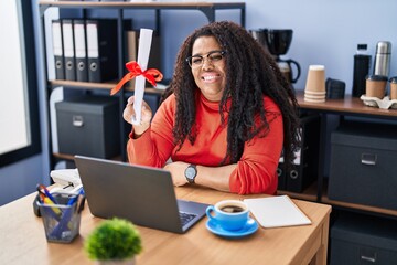 Fototapeta na wymiar Plus size hispanic woman working at the office holding diploma looking positive and happy standing and smiling with a confident smile showing teeth