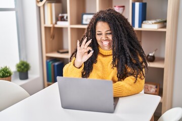 Plus size hispanic woman using laptop at home doing ok sign with fingers, smiling friendly gesturing excellent symbol