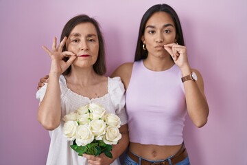 Hispanic mother and daughter holding bouquet of white flowers mouth and lips shut as zip with...
