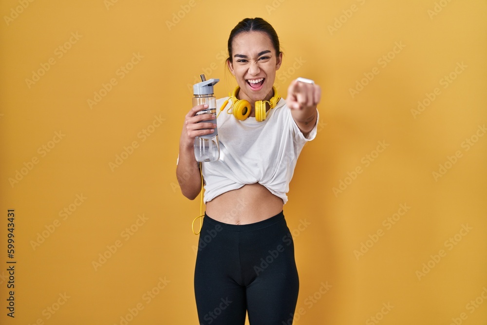 Poster Young south asian woman wearing sportswear drinking water pointing to you and the camera with fingers, smiling positive and cheerful