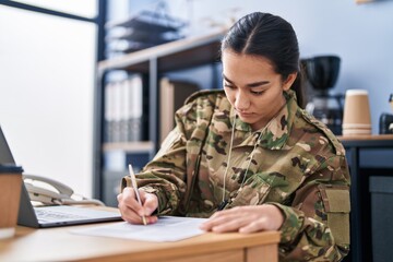 Young hispanic woman army soldier using laptop writing on document at office