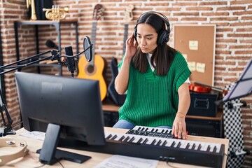 Young hispanic woman musician playing piano keyboard at music studio