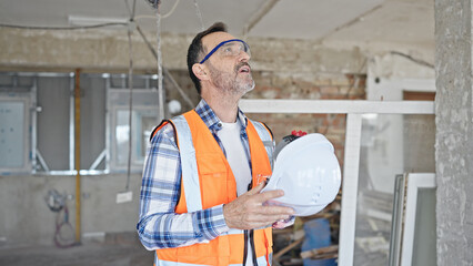 Middle age man builder tired using hardhat as a hand fan at construction site