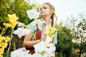 Portrait of adorable teenager girl with cute hairstyle wearing overalls taking care and enjoy beautiful flowers in the garden.