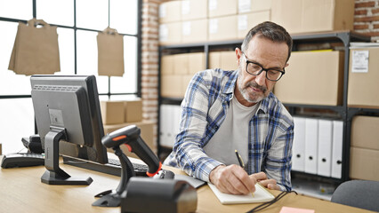 Middle age man ecommerce business worker using computer writing on package at office