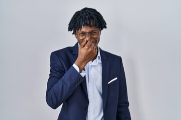 Young african man with dreadlocks wearing business jacket over white background smelling something...