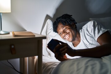 Fototapeta premium African american man using smartphone lying on bed at bedroom