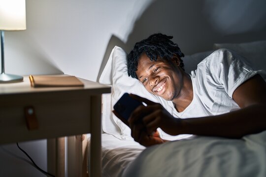 African american man using smartphone lying on bed at bedroom