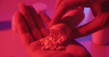 Man taking pills out of can in neon light, representing modern drug and medicine addiction - Dystopia concept close up 