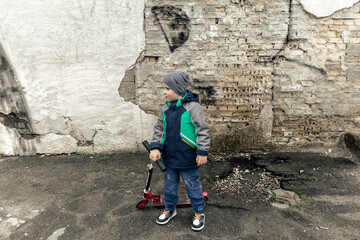 A little boy with a scooter on the background of a broken brick wall