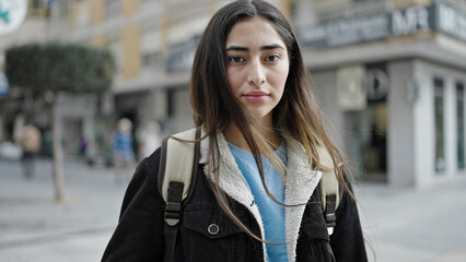 Young beautiful hispanic woman student standing with serious expression at street