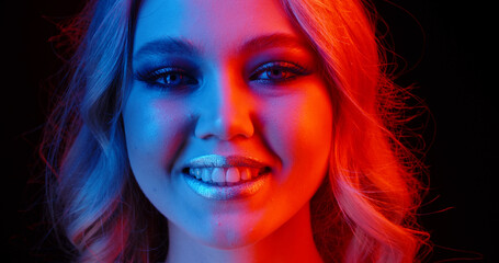 Beautiful caucasian girl with bright makeup making a positive smile in red and blue neon light - emotions, nightlife concept close up shot
