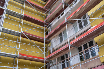 Insulating exterior by Mineral material, working on facade of old appartment building in Europe. Renovation Building work  on Construction site. Scaffolding around the wall.