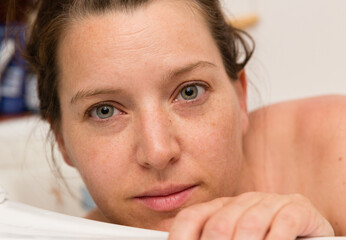 woman looks out of the bathtub, her hand on the edge without make-up, with a slight smile on her lips