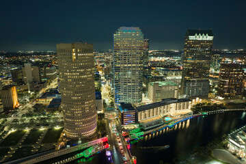 Fototapeta premium View from above of illuminated skyscraper buildings, pedestrian riverwalk and street traffic in downtown of Tampa city in Florida, USA. American megapolis with business financial district at night