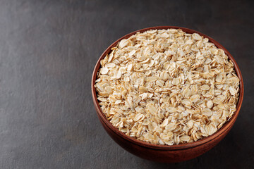 Oat flakes in a clay bowl on a dark background. Organic rolled oats for healthy nutrition. Copy space. Top view