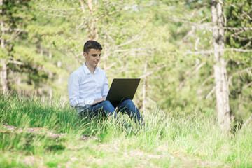 young man sits in the park and works on a laptop