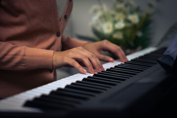 Fototapeta premium Croped Asian woman hand put on piano key to preparing to play music, closed up girl hand on music instrument with blur flower background.
