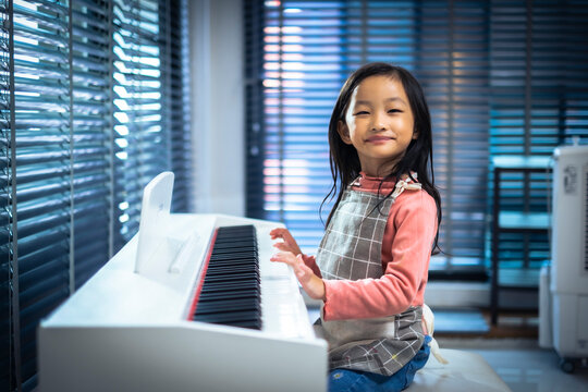 Asian litle girl sitting in front of piano smile to camera with inocent feeling, child interested in playing piano.