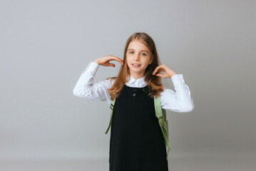cheerful teenage girl 11,12,13 years old in a school uniform wears a backpack on a gray background. school fashion