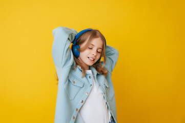 A young girl 11-13 years old in headphones listens to music and dances in the studio on a yellow background