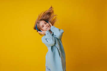 A young girl 11-13 years old in headphones listens to music and dances in the studio on a yellow background