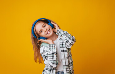 A young girl 11-13 years old in headphones listens to music and dances in the studio on a yellow background