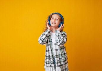 A young girl 11-13 years old in headphones listens to music and dances in the studio on a yellow background