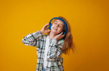 A young girl 11-13 years old in headphones listens to music and dances in the studio on a yellow background