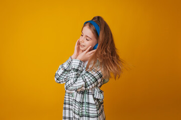 A young girl 11-13 years old in headphones listens to music and dances in the studio on a yellow background