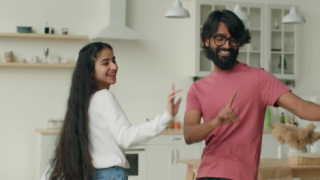 Arabian husband dance with indian wife happy carefree ethnic couple dancers dancing in home kitchen listen music smiling woman girl and man guy have fun celebrate weekend relocation to rented house