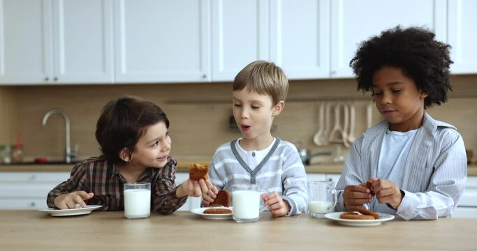 Cheerful cute diverse kids eating sugar free organic bakery foods, cookies, biscuits, having healthy snacks for break, drinking milk, talking, laughing, caring for nutrition