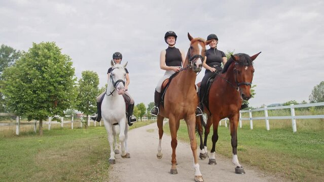 Three smiling young women, recreational jockeys enjoying an equestrian leisure ride on beautiful horses, front view. Horseback riding concept.