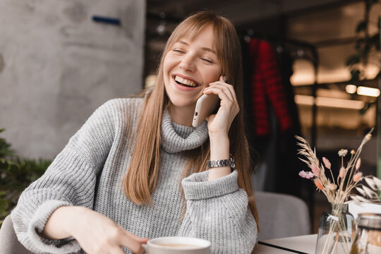 Blonde woman smiling positive conversation talking to her friend using phone hand hold hot drink tea relax casual positive emotion weekend relax routine at cafe restaurant. Girl have discussion.
