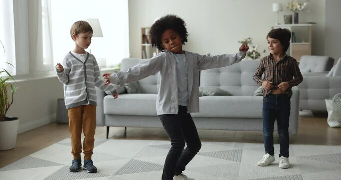 Talented African dancer boy teaching diverse friends to dance at home, showing action performance, movement to repeat, training multiethnic fellows. Group of kids learning contemporary dance