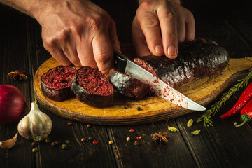 Cutting blood sausage with a knife in the hands of a cook on a cutting board. Cooking a national...