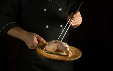 Professional chef prepares lunch with raw chicken leg on the cutting board of the restaurant kitchen. Delicious idea for grilling on black background