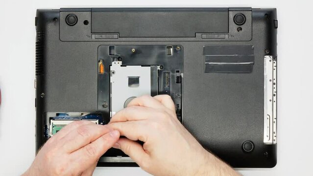 Disassembling a laptop. Repairman removes the hard drive. The master electronics engineer unscrews the screws and removes the Solid-state drive SSD from the computer. Warranty repair in the workshop