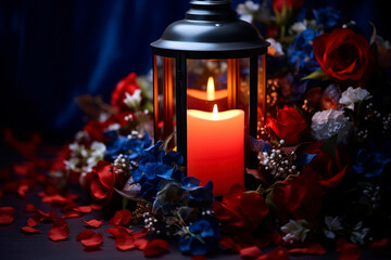 Solitary lit candle within a glass lantern, surrounded by a wreath of red, white, and blue flowers, paying tribute to fallen heroes on Memorial Day.