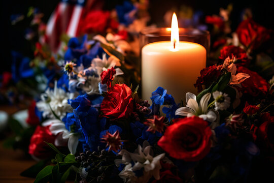 Solitary lit candle within a glass lantern, surrounded by a wreath of red, white, and blue flowers, paying tribute to fallen heroes on Memorial Day.